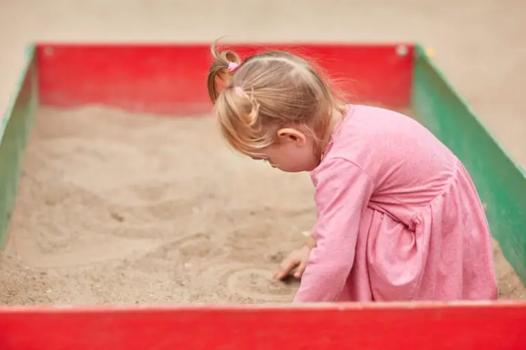 Little girl in a pink dress in a sandbox.